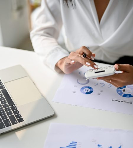 Cropped image of a businesswoman or female accountant using calculator to calculate sales, working at her desk in the office.